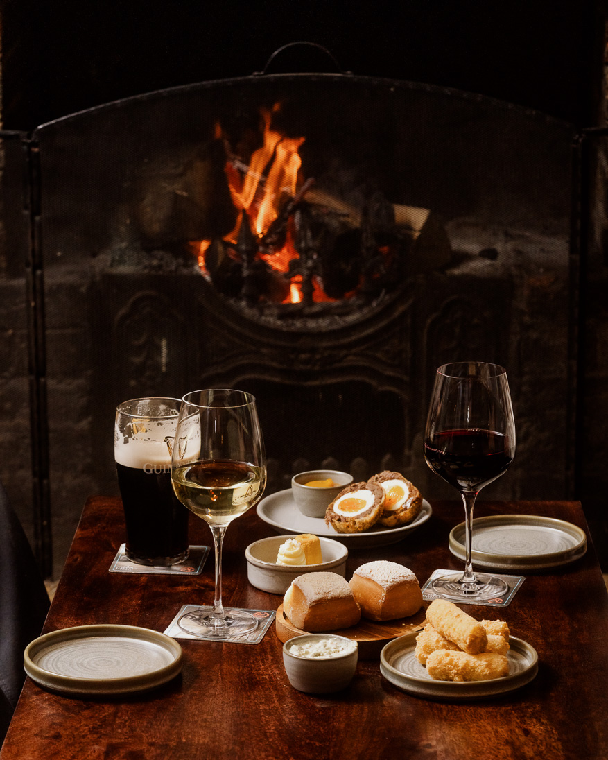 Two glasses of wine with a pint of Guinness, and selection of food by fire